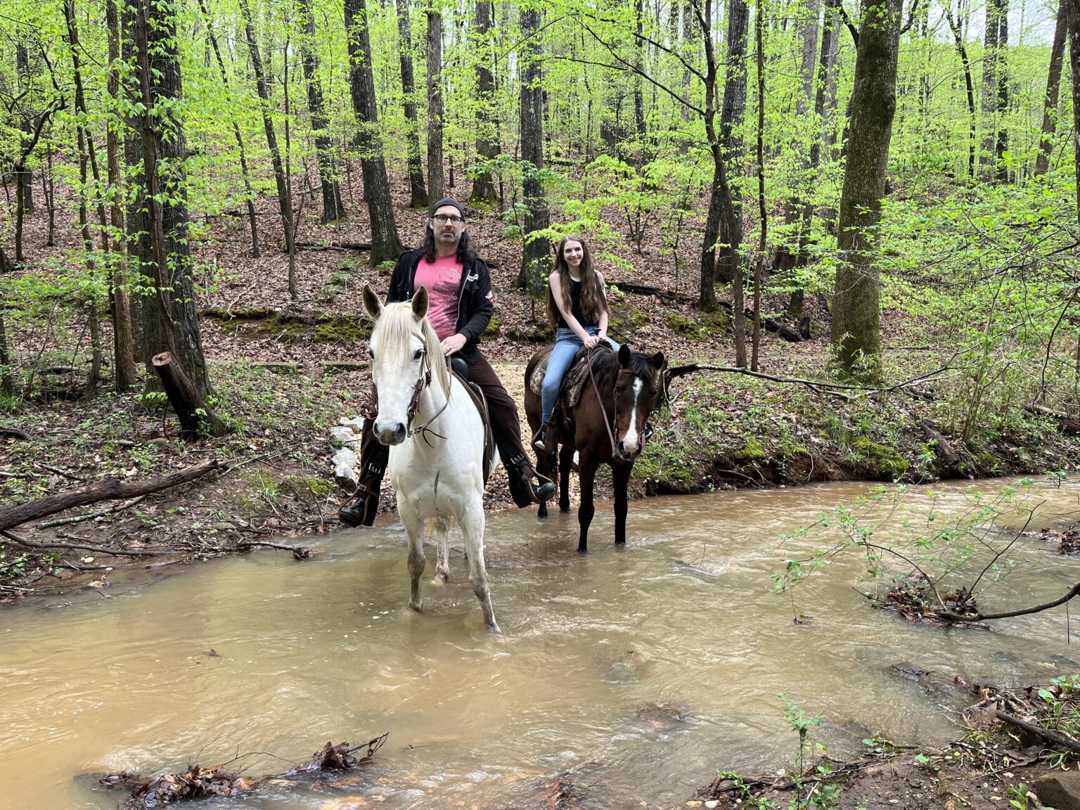 Riders crossing a creek on a wooded trail